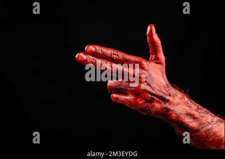 Blutige männliche Hand zeigt eine Waffe vor schwarzem Hintergrund. Stockfoto