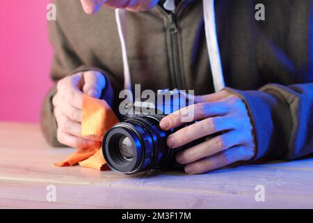 Reinigungstuch der digitalen spiegelreflexkamera mit manuellem, altem Objektiv durch eine Person auf farbigem Hintergrund Stockfoto