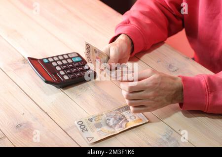 Zählen polnischer Zloty-Banknoten mit Taschenrechner auf dem Tisch und farbigem Hintergrund Stockfoto