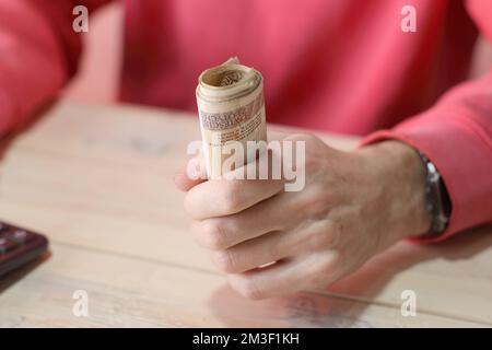 Eine Rolle polnischer Zloty-Banknoten in der Hand einer Person in einem roten Sweatshirt über dem Tisch Stockfoto