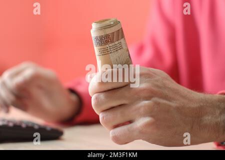 Eine Rolle polnischer Zloty-Banknoten in der Hand einer Person in einem roten Sweatshirt über dem Tisch Stockfoto