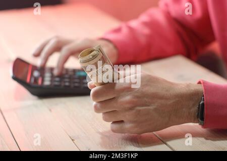 Eine Rolle polnischer Zloty-Banknoten in der Hand einer Person in einem roten Sweatshirt über dem Tisch Stockfoto