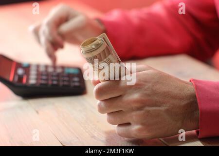 Eine Rolle polnischer Zloty-Banknoten in der Hand einer Person in einem roten Sweatshirt über dem Tisch Stockfoto