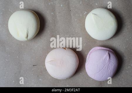 Vier farbenfrohe, handgemachte Marshmallows auf handwerklichem Papier auf dem Tisch Stockfoto