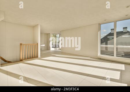 Ein leeres Wohnzimmer mit weißem Fliesenboden und großen Fenstern mit Blick auf die Straße vor dem Haus Stockfoto