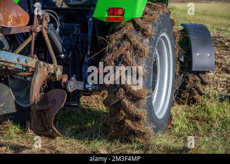 Landwirtschaftskonzept. Traktor mit Pflug, Nahaufnahme des mit Schlamm bedeckten Rads, nicht kultivierter Landwirtschaftsbetrieb. Die landwirtschaftliche Saison hat begonnen. Stockfoto