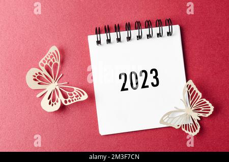 2023 Tischkalender und Schmetterling aus Papier auf rotem Hintergrund. Stockfoto