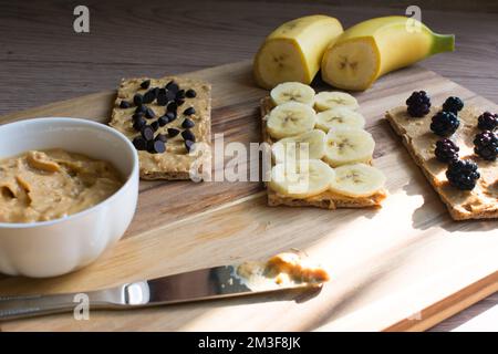 Erdnussbutter in Schüssel, Präsentation von Früchten mit Erdnussbutter auf einem Holzbrett, gesunde Ernährung und Bio-Lebensmittel. Stockfoto