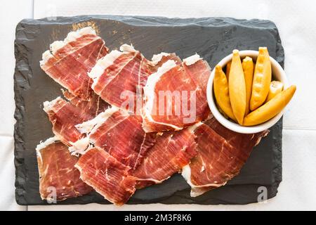 Blick von oben auf den köstlichen iberischen oder iberischen Schinken, serviert auf einem Teller mit Crackerbrot Stockfoto