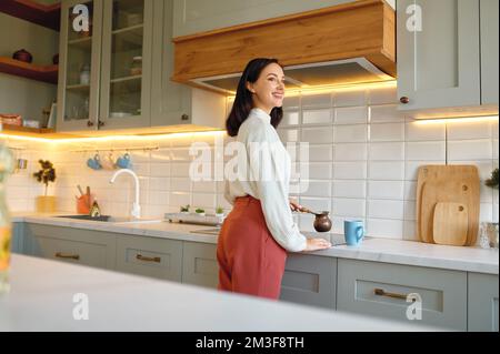 Glückliche junge Frau, die Kaffee in einer Cezve-Tasse in der Küche kocht Stockfoto