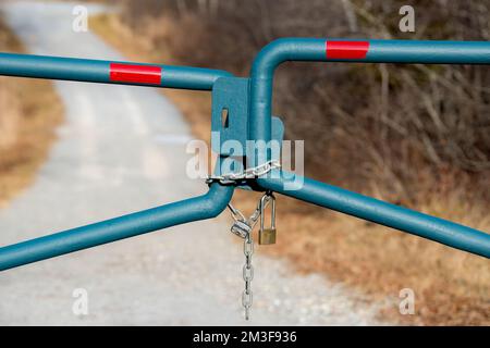 Verriegeltes Tor blockiert Schotterstraße. Zwei Vorhängeschlösser sichtbar. Rotes reflektierendes Warnband oben. Konzentrieren Sie sich auf den oberen Teil der Kette. Stockfoto