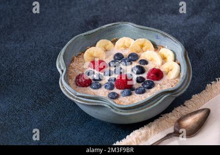 Pflanzliches Frühstück aus Stahlhafer, garniert mit Banane, Heidelbeeren, Himbeeren, gemischt mit Mandelmilch Stockfoto