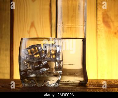 Glas Rum mit Eis auf dem Flaschenhintergrund und einem Holzhintergrund Stockfoto