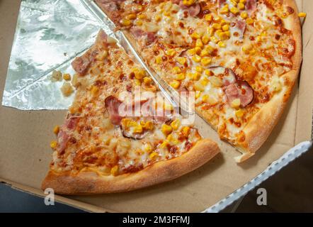 Pizzastücke mit Speck und Mais in einer offenen Pappschachtel, Draufsicht Stockfoto