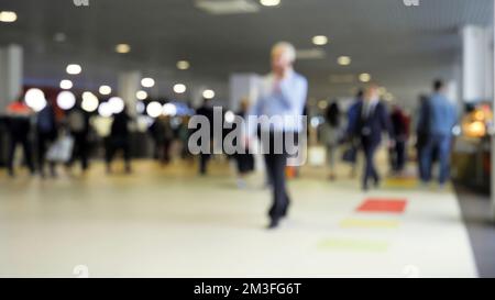 Verschwommener Blick auf die Leute, die durch die Lobby gehen. Medien. Viele Leute laufen im Einkaufszentrum herum. Verschiedene Leute und Geschäftsleute gehen durch die Geschäfte oder Businessläden Stockfoto