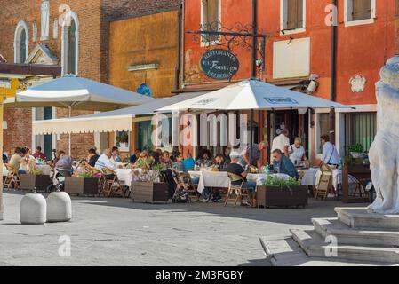 Restaurant piazza Italy, Blick im Sommer auf eine Gruppe von Menschen, die außerhalb einer Pizzeria im malerischen Hafen von Chioggia, Comune of Venice, Italien, essen Stockfoto