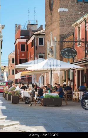 Speisen und Getränke aus Chioggia, im Sommer sehen Sie eine Gruppe von Menschen, die außerhalb einer Pizzeria im malerischen Hafen von Chioggia, Comune of Venice, Italien, essen Stockfoto