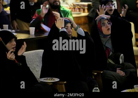 Teheran, Teheran, Iran. 14.. Dezember 2022. Getarnte iranische Fans reagieren auf das Halbfinale der FIFA-Weltmeisterschaft Katar 2022 zwischen Frankreich und Marokko im Nakhlestan Café im Zentrum von Teheran, Iran, am 14. Dezember 2022. Fans aus dem Iran, dem Libanon, dem Jemen, Syrien und Palästina versammeln sich im Nakhlestan Cafe, das vom Owj, der Arts and Media Organization des Islamic Revolutionary Guard Corps (IRGS), betrieben wird und sich im Besitz der Organisation für Kunst und Medien befindet, um die marokkanische Nationalmannschaft zu unterstützen. Nach dem Sieg gegen Portugal in Katar am 10.. Dezember trugen die Marokkaner palästinensische Flaggen, um ihre Unterstützung für Pale zu zeigen Stockfoto