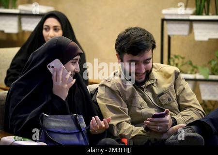 Teheran, Teheran, Iran. 14.. Dezember 2022. Ein iranisches Paar sieht am 14. Dezember 2022 im Nakhlestan Café im Zentrum von Teheran, Iran, eine Live-Übertragung des Halbfinalspiels der Katar-Weltmeisterschaft 2022 zwischen Marokko und Frankreich. Fans aus dem Iran, dem Libanon, dem Jemen, Syrien und Palästina versammeln sich im Nakhlestan Cafe, das vom Owj, der Arts and Media Organization des Islamic Revolutionary Guard Corps (IRGS), betrieben wird und sich im Besitz der Organisation für Kunst und Medien befindet, um die marokkanische Nationalmannschaft zu unterstützen. Nach dem Sieg gegen Portugal in Katar am 10.. Dezember trugen die Marokkaner palästinensische Flaggen, um ihre Unterstützung für die Palästinenser zu zeigen. Stockfoto