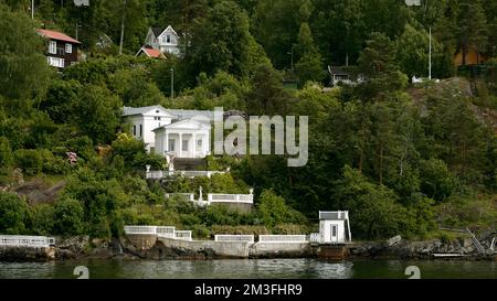 Blick vom See auf grüne Büsche und Bäume und ein Gebäude im Inneren. Aktie-Aufnahmen. Sommerlandschaft mit Häusern und grüner Vegetation Stockfoto