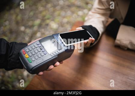 Verkürzter Blick auf eine Frau, die mit dem Handy im Café im Freien bezahlt, Bild von der Börse Stockfoto