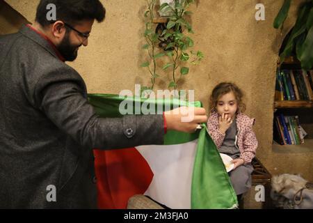 Teheran, Teheran, Iran. 14.. Dezember 2022. Ein iranischer Fan hält eine palästinensische Flagge (L), während er das Nakhlestan Café in der Innenstadt von Teheran besucht, um das Halbfinale der FIFA Weltmeisterschaft Katar 2022 zwischen Frankreich und Marokko am 14. Dezember 2022 auf der Leinwand zu sehen. Fans aus dem Iran, dem Libanon, dem Jemen, Syrien und Palästina versammeln sich im Nakhlestan Cafe, das vom Owj, der Arts and Media Organization des Islamic Revolutionary Guard Corps (IRGS), betrieben wird und sich im Besitz der Organisation für Kunst und Medien befindet, um die marokkanische Nationalmannschaft zu unterstützen. Nach dem Sieg gegen Portugal in Katar am 10.. Dezember trugen die Marokkaner palästinensische Flaggen, um ihre Unterstützung zu zeigen Stockfoto