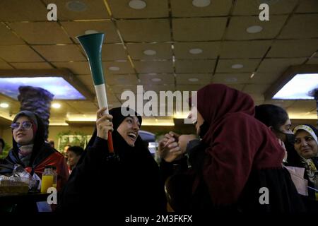 Teheran, Teheran, Iran. 15.. Dezember 2022. Getarnte iranische Fans reagieren, während einer von ihnen ein Horn hält, während er das Halbfinale der FIFA-Weltmeisterschaft Katar 2022 zwischen Frankreich und Marokko am 15. Dezember 2022 im Nakhlestan Café im Zentrum von Teheran, Iran, auf dem Bildschirm sieht. Fans aus dem Iran, dem Libanon, dem Jemen, Syrien und Palästina versammeln sich im Nakhlestan Cafe, das vom Owj, der Arts and Media Organization des Islamic Revolutionary Guard Corps (IRGS), betrieben wird und sich im Besitz der Organisation für Kunst und Medien befindet, um die marokkanische Nationalmannschaft zu unterstützen. Nach dem Sieg gegen Portugal in Katar am 10.. Dezember trugen die Marokkaner palästinensische Flaggen nach Katar Stockfoto