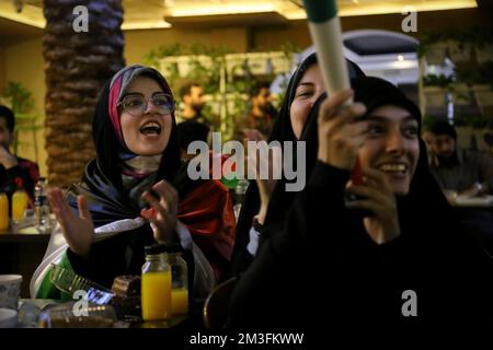 Teheran, Teheran, Iran. 15.. Dezember 2022. Getarnte iranische Fans reagieren, während einer von ihnen ein Horn hält, während er das Halbfinale der FIFA-Weltmeisterschaft Katar 2022 zwischen Frankreich und Marokko am 15. Dezember 2022 im Nakhlestan Café im Zentrum von Teheran, Iran, auf dem Bildschirm sieht. Fans aus dem Iran, dem Libanon, dem Jemen, Syrien und Palästina versammeln sich im Nakhlestan Cafe, das vom Owj, der Arts and Media Organization des Islamic Revolutionary Guard Corps (IRGS), betrieben wird und sich im Besitz der Organisation für Kunst und Medien befindet, um die marokkanische Nationalmannschaft zu unterstützen. Nach dem Sieg gegen Portugal in Katar am 10.. Dezember trugen die Marokkaner palästinensische Flaggen nach Katar Stockfoto