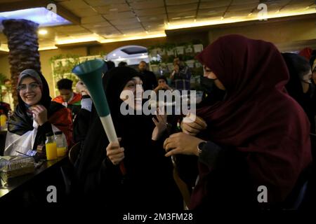 Teheran, Teheran, Iran. 15.. Dezember 2022. Getarnte iranische Fans reagieren, während einer von ihnen ein Horn hält, während er das Halbfinale der FIFA-Weltmeisterschaft Katar 2022 zwischen Frankreich und Marokko am 15. Dezember 2022 im Nakhlestan Café im Zentrum von Teheran, Iran, auf dem Bildschirm sieht. Fans aus dem Iran, dem Libanon, dem Jemen, Syrien und Palästina versammeln sich im Nakhlestan Cafe, das vom Owj, der Arts and Media Organization des Islamic Revolutionary Guard Corps (IRGS), betrieben wird und sich im Besitz der Organisation für Kunst und Medien befindet, um die marokkanische Nationalmannschaft zu unterstützen. Nach dem Sieg gegen Portugal in Katar am 10.. Dezember trugen die Marokkaner palästinensische Flaggen nach Katar Stockfoto