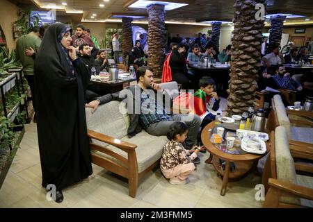 Teheran, Teheran, Iran. 15.. Dezember 2022. Eine iranische Familie sieht am 15. Dezember 2022 im Nakhlestan Café im Zentrum von Teheran, Iran, eine Live-Übertragung des Halbfinalspiels der Katar-Weltmeisterschaft 2022 zwischen Marokko und Frankreich. Fans aus dem Iran, dem Libanon, dem Jemen, Syrien und Palästina versammeln sich im Nakhlestan Cafe, das vom Owj, der Arts and Media Organization des Islamic Revolutionary Guard Corps (IRGS), betrieben wird und sich im Besitz der Organisation für Kunst und Medien befindet, um die marokkanische Nationalmannschaft zu unterstützen. Nach dem Sieg gegen Portugal in Katar am 10.. Dezember trugen die Marokkaner palästinensische Flaggen, um ihre Unterstützung für die Palästinenser zu zeigen. Stockfoto