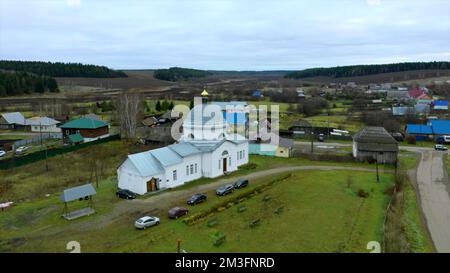 Luftaufnahme einer traditionellen orthodoxen Kirche in einem Sommerdorf. Clip. Fliegen Sie über die Landschaft mit kleinen Häusern Stockfoto