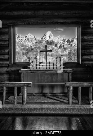 Berge durch Glasfenster über dem Altar der historischen Kapelle der Transfiguration im Grand Teton National Park in der Nähe von Moose, Wyoming Stockfoto