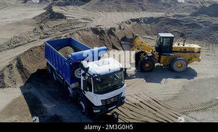 USA, Arkansas - 28. Juni 2022: Sandsteinbruch, industrielle Sandgewinnung für die Bauindustrie. Szene. Traktoren laden Sand in Kipplaster, Minin Stockfoto