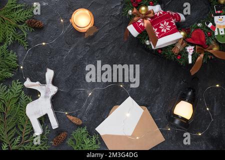 Weihnachtskomposition. Geschenke, Umschlag, Tannenäste, weiße Dekorationen auf schwarzem Hintergrund. Stockfoto