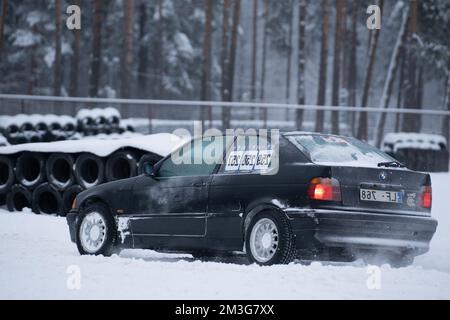 12-12-2022 Riga, Lettland ein Auto steht im Schnee neben einem Haufen Reifen und einem Zaun mit einem Schild. . Stockfoto
