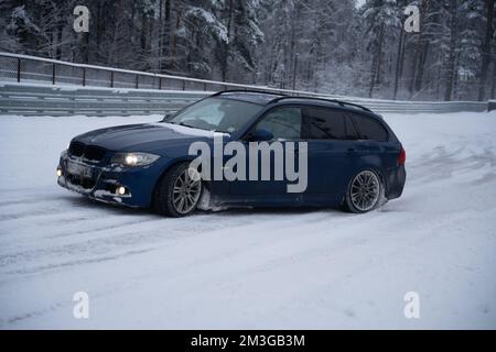 12-12-2022 Riga, Lettland ein blaues Auto steht im Schnee neben einem Zaun und Bäumen im Hintergrund. . Stockfoto