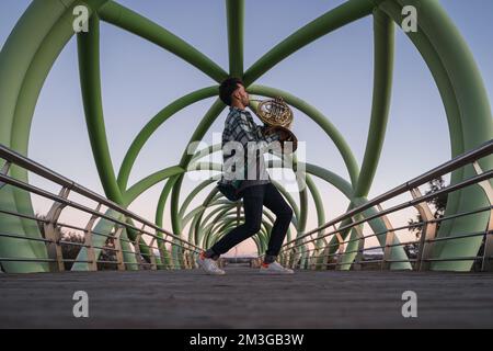 Ein Musiker, der mit seinem Horn in der Hand auf einer Brücke läuft. Stockfoto