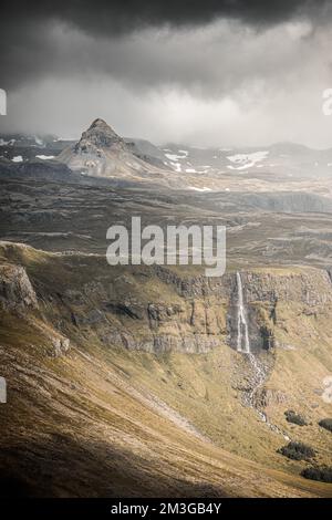 Eine vertikale Luftaufnahme des Wasserfalls Bjarnafoss, der an einem bewölkten Tag in Island die Klippe hinunterfällt Stockfoto