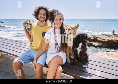 Mann und Frau Paar lächeln selbstbewusst und umarmen sich am Meer mit Hunden Stockfoto
