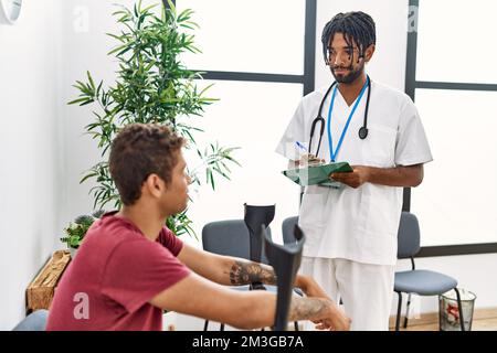 Zwei Männer Physiotherapeuten und Patienten, die medizinische Beratung mit Krücken im Wartezimmer des Krankenhauses Stockfoto