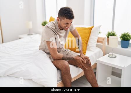 Ein afroamerikanischer Mann, der an Knieschmerzen leidet, sitzt im Bett im Schlafzimmer Stockfoto