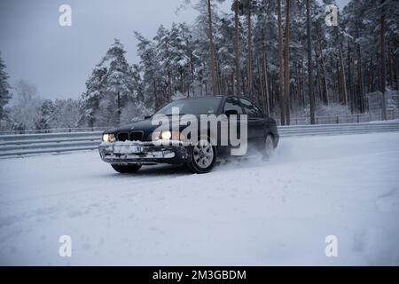 12-12-2022 Riga, Lettland ein Auto fährt durch eine schneebedeckte Straße vor einem Wald von Bäumen und einem Zaun mit Schnee. . Stockfoto