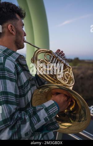 Ein Mann, der mit seinem Musikinstrument auf einer grünen Rohrbrücke läuft. Er hält ein goldenes Horn in der Hand. Das Licht ist sehr dunkel, weil es getti ist Stockfoto