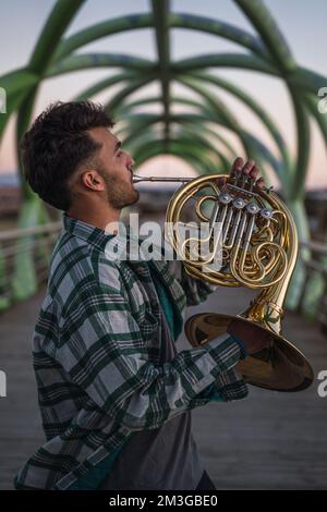 Ein Mann, der mit seinem Musikinstrument auf einer grünen Rohrbrücke läuft. Er hält ein goldenes Horn in der Hand. Das Licht ist sehr dunkel, weil es getti ist Stockfoto