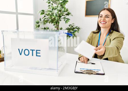 Junge schöne hispanische Frau Wahltisch Präsident hält Stimmpapier an Wahlkollegium Stockfoto