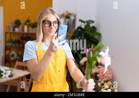 Junge blonde Frau Floristin machen Foto, um mit dem Smartphone im Blumenladen zu blühen Stockfoto