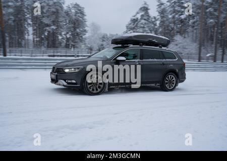 12-12-2022 Riga, Lettland ein Auto mit einem Surfbrett im Schnee, mit Bäumen im Hintergrund und einer schneebedeckten Straße. . Stockfoto