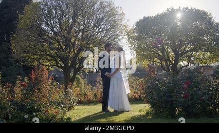 Hochzeitsfotos im Sommerwald. Action. Ein schönes, emotionales, lächelndes junges Paar wird fotografiert und küsst sich in einem grünen Garten. Hohe Qualität Stockfoto
