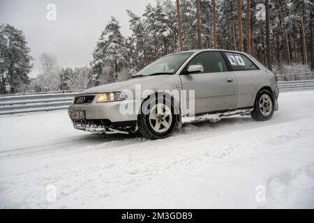 12-12-2022 Riga, Lettland ein Auto fährt durch den Schnee in einem bewaldeten Gebiet mit Bäumen im Hintergrund und einem Zaun im Vordergrund. . Stockfoto