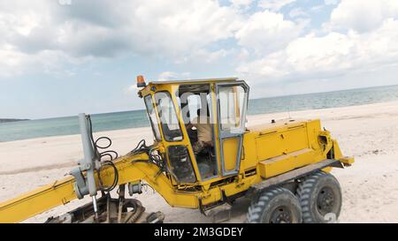 Baustelle für Bulldozer. Schuss. Draufsicht auf Bulldozer, die auf dem Meer am Strand fahren. Sandbergbau oder Baustelle an der Küste. Stockfoto